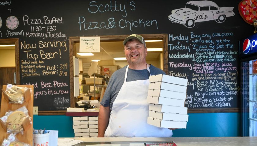 Owner at Scotty’s Pizza & Chicken in Marshfield Wisconsin holding pizza boxes at counter